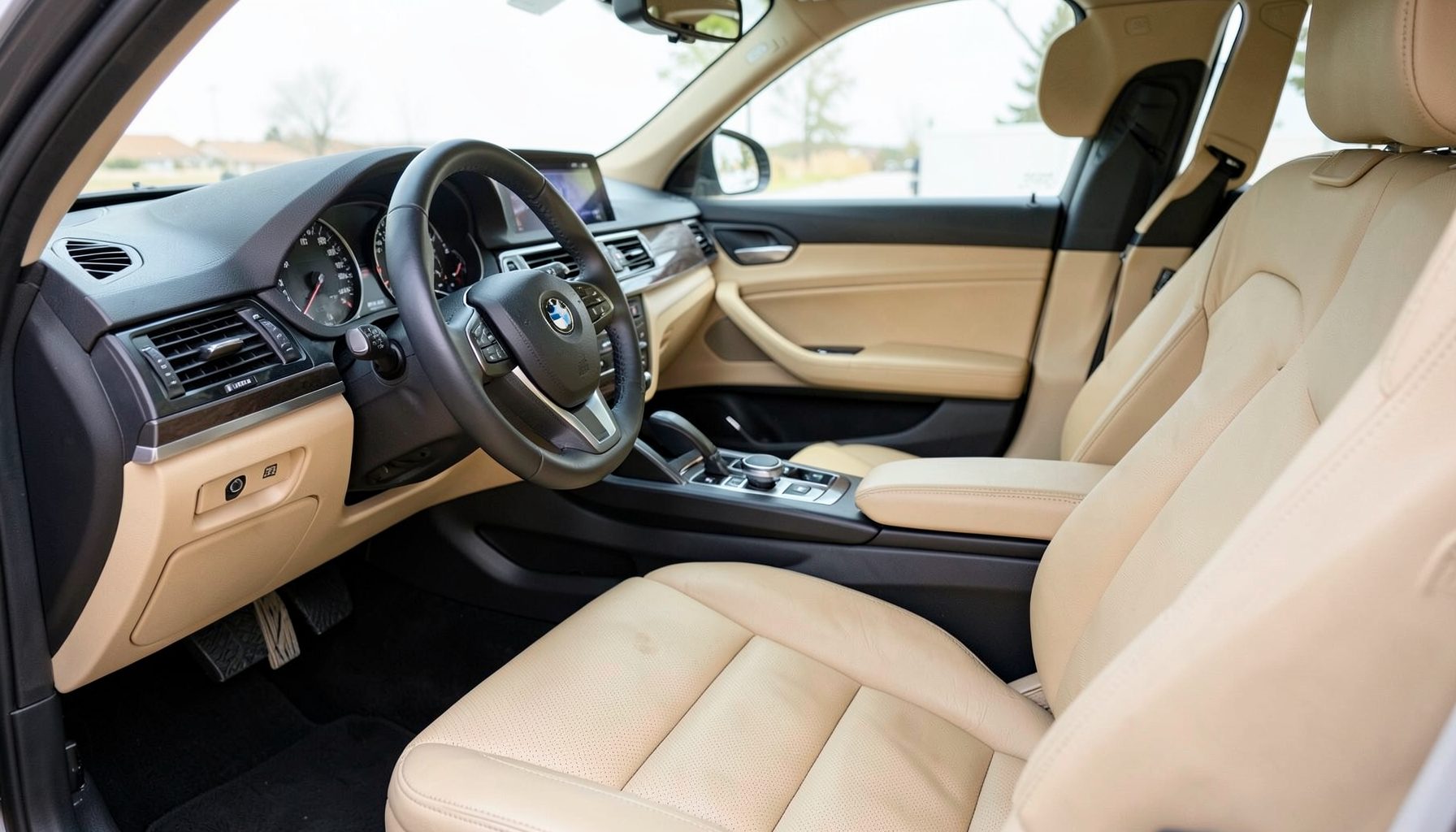 Светлый салон автомобиля BMW с кожаными сиденьями и приборной панелью, тёплые бежевые и чёрные тона, чистота и уют